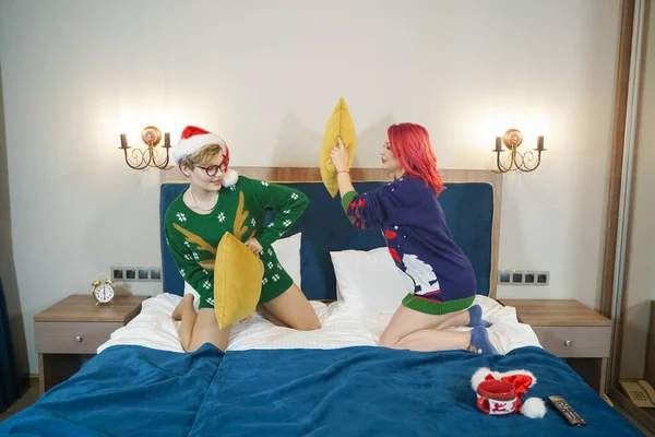 Dois bonito meninas felizes amigos têm travesseiro luta em camisolas de Natal na grande cama azul — Fotografia de Stock