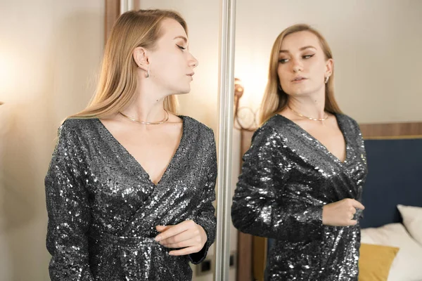 Flicka försöker klä sig i spegeln glad och glad. Söt vacker vit ung kvinna i svart glitter aftonklänning. — Stockfoto