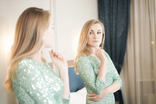 Bela jovem mulher em apertado curto brilho vestido de noite pronto para a festa e olhando para o espelho em si mesmo — Fotografia de Stock