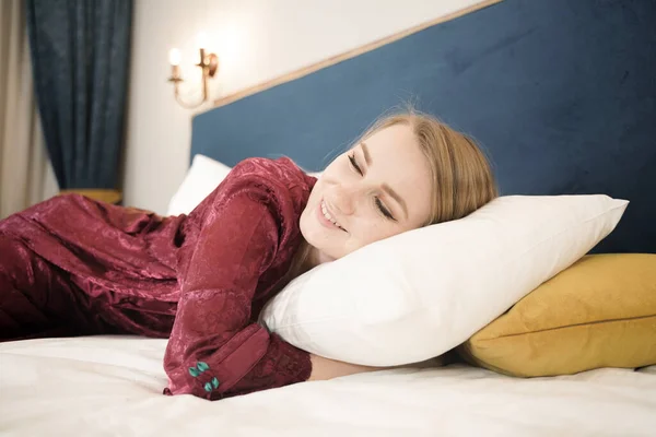 Menina em roupão vermelho escuro relaxar na cama em seu quarto sozinho e alegre — Fotografia de Stock