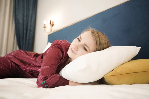 Menina em roupão vermelho escuro relaxar na cama em seu quarto sozinho e alegre — Fotografia de Stock