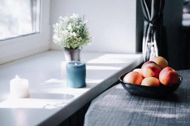 Masanın üzerinde beyaz pencerenin önünde bir tabak şeftali var.