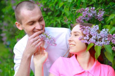 Oğlan ve kız, yazın parkta leylak çiçekleriyle poz veriyorlar.
