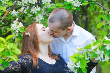 Meyve bahçesindeki genç çift çiçek dallarıyla birlikte yürüyor ve bir randevuları var.