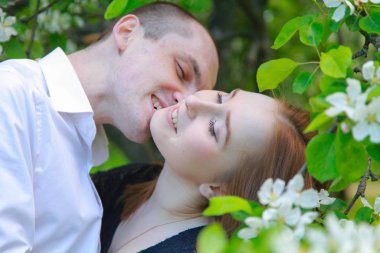 Meyve bahçesindeki genç çift çiçek dallarıyla birlikte yürüyor ve bir randevuları var.