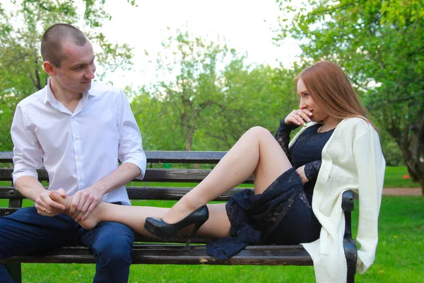 Romantic couple on a bench hugs and enjoys together in love. a man gives a girl a foot massage — Stock Photo, Image