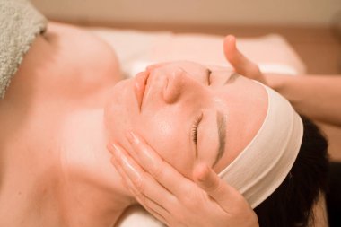 Güzel genç bir kadın güzellik salonunda yüz masajı yaptırıyor.