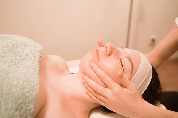 Hermosa joven recibiendo un tratamiento de masaje facial en el salón de belleza — Foto de Stock