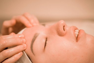 Güzel genç bir kadın güzellik salonunda yüz masajı yaptırıyor.