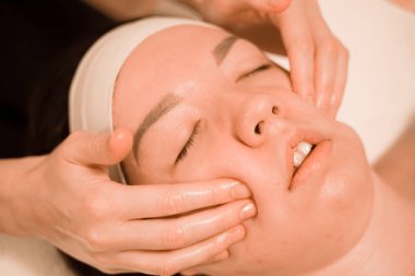 Güzel genç bir kadın güzellik salonunda yüz masajı yaptırıyor.