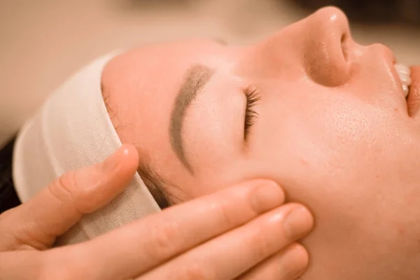 Hermosa joven recibiendo un tratamiento de masaje facial en el salón de belleza —  Fotos de Stock