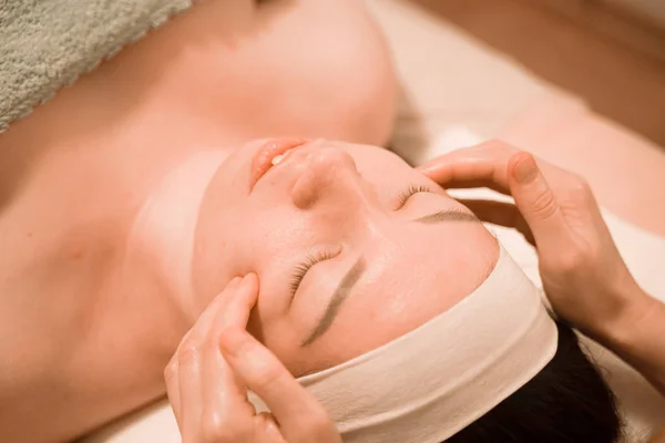 Hermosa joven recibiendo un tratamiento de masaje facial en el salón de belleza —  Fotos de Stock