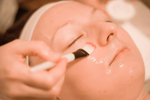 Mujer joven acostada en el salón de spa mientras hace mascarilla facial por cepillo. de cerca —  Fotos de Stock