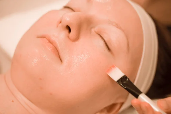 Молодая женщина лежит в спа-салоне, делая маску для лица за кистью. close up — стоковое фото