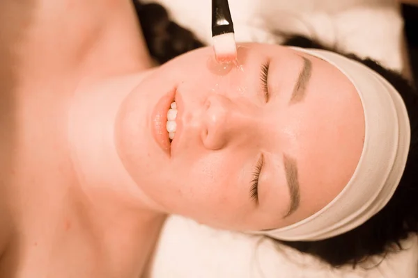Söt mix ras kvinna ligger och njuter av processen att tillämpa en pensel mask i skönhetssalongen i ansiktet — Stockfoto