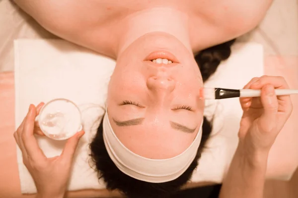 Linda mezcla de raza mujer miente y disfruta del proceso de aplicación de una máscara de cepillo en el salón de belleza en su cara — Foto de Stock