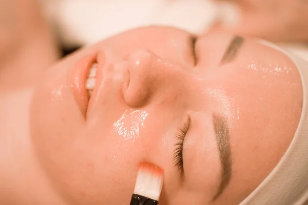 Söt mix ras kvinna ligger och njuter av processen att tillämpa en pensel mask i skönhetssalongen i ansiktet — Stockfoto