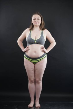 Artı boy kadın vücudunu selülit izleriyle ve saçlarıyla gösteriyor ve kendini sevmen ve kabullenmen için seni cesaretlendiriyor. Stüdyoda siyah arka plan. tam boy fotoğraf