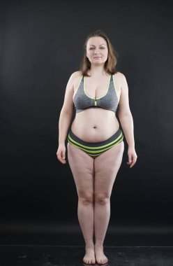 Artı boy kadın vücudunu selülit izleriyle ve saçlarıyla gösteriyor ve kendini sevmen ve kabullenmen için seni cesaretlendiriyor. Stüdyoda siyah arka plan. tam boy fotoğraf