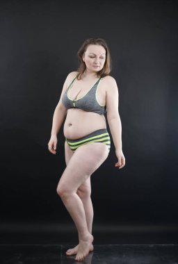 Artı boy kadın vücudunu selülit izleriyle ve saçlarıyla gösteriyor ve kendini sevmen ve kabullenmen için seni cesaretlendiriyor. Stüdyoda siyah arka plan. tam boy fotoğraf