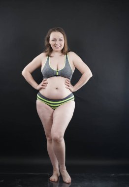 Artı boy kadın vücudunu selülit izleriyle ve saçlarıyla gösteriyor ve kendini sevmen ve kabullenmen için seni cesaretlendiriyor. Stüdyoda siyah arka plan. tam boy fotoğraf