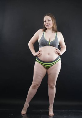 Artı boy kadın vücudunu selülit izleriyle ve saçlarıyla gösteriyor ve kendini sevmen ve kabullenmen için seni cesaretlendiriyor. Stüdyoda siyah arka plan. tam boy fotoğraf