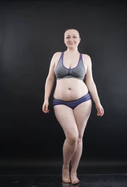 Artı boy kadın vücudunu selülit izleriyle ve saçlarıyla gösteriyor ve kendini sevmen ve kabullenmen için seni cesaretlendiriyor. Stüdyoda siyah arka plan. tam boy fotoğraf