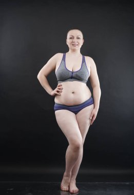 Artı boy kadın vücudunu selülit izleriyle ve saçlarıyla gösteriyor ve kendini sevmen ve kabullenmen için seni cesaretlendiriyor. Stüdyoda siyah arka plan. tam boy fotoğraf