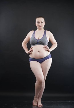 Artı boy kadın vücudunu selülit izleriyle ve saçlarıyla gösteriyor ve kendini sevmen ve kabullenmen için seni cesaretlendiriyor. Stüdyoda siyah arka plan. tam boy fotoğraf