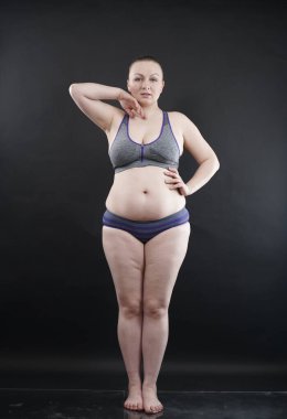 Artı boy kadın vücudunu selülit izleriyle ve saçlarıyla gösteriyor ve kendini sevmen ve kabullenmen için seni cesaretlendiriyor. Stüdyoda siyah arka plan. tam boy fotoğraf