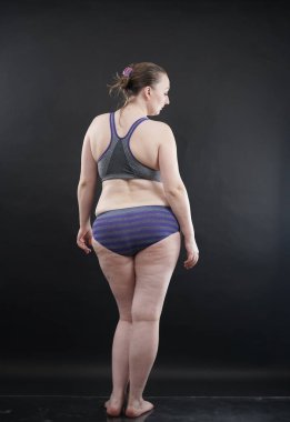 Artı boy kadın vücudunu selülit izleriyle ve saçlarıyla gösteriyor ve kendini sevmen ve kabullenmen için seni cesaretlendiriyor. Stüdyoda siyah arka plan. tam boy fotoğraf