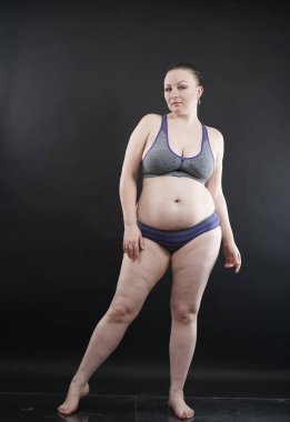 Artı boy kadın vücudunu selülit izleriyle ve saçlarıyla gösteriyor ve kendini sevmen ve kabullenmen için seni cesaretlendiriyor. Stüdyoda siyah arka plan. tam boy fotoğraf