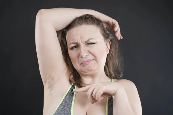woman shows her unshaved armpit. plus size middle age woman is not happy with hair in her armpits. Caucasian girl is emotional sad and upset. black background in the photo Studio.
