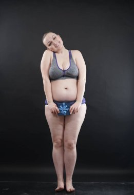 Spor iç çamaşırı giyen güzel ve cüsseli bir kadın siyah stüdyo sağlam arka planda bir spor salonuna hediye aboneliği olan bir kutu tutuyor.