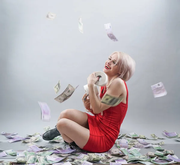 caucasian emotional blonde girl in red dress holds toilet paper and enjoys life in the rain of money. a rich woman is ready to stay at home during an epidemic covid and happy. white studio background