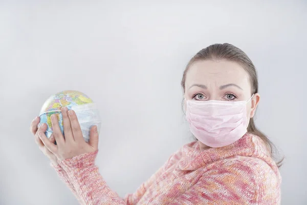 Putting a green surgical face mask on the globe sphere model. Heal the world concept. Woman in medical mask holds world globe with covid-19 coronavirus desease.