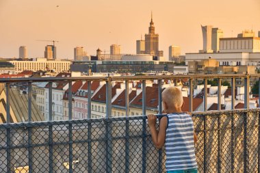 Warsaw, Poland - August 11, 2017: Little boy looks at beautiful panoramic view over the roofs of the Old Town to the Center of Warsaw, the Palace of culture and science (PKiN), modern skyscrapers and  clipart