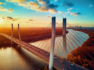 Vistula nehri ve Varşova şehri gökdelenleri üzerindeki Siekierkowski Köprüsü 'ne güzel panoramik hava aracı görüntüsü Kasım akşamı günbatımında Polonya' nın altın kırmızısı sonbahar renklerinde.