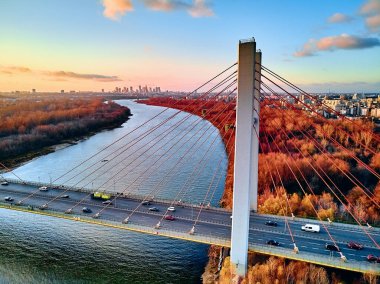 Vistula nehri ve Varşova şehri gökdelenleri üzerindeki Siekierkowski Köprüsü 'ne güzel panoramik hava aracı görüntüsü Kasım akşamı günbatımında Polonya' nın altın kırmızısı sonbahar renklerinde.
