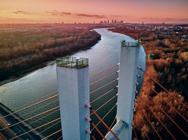 Beautiful panoramic aerial drone view to cable-stayed Siekierkowski Bridge over the Vistula river and Warsaw City skyscrapers, Poland in gold red autumn colors in November evening at sunset clipart