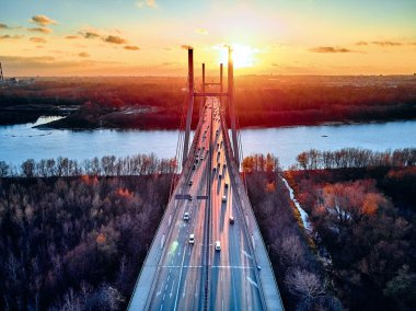 Beautiful panoramic aerial drone view to cable-stayed Siekierkowski Bridge over the Vistula river and Warsaw City skyscrapers, Poland in gold red autumn colors in November evening at sunset clipart