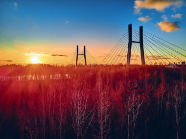 Vistula nehri ve Varşova şehri gökdelenleri üzerindeki Siekierkowski Köprüsü 'ne güzel panoramik hava aracı görüntüsü Kasım akşamı günbatımında Polonya' nın altın kırmızısı sonbahar renklerinde.