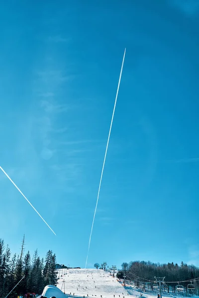 Condensation trail (Inversion trail, jet trail) of an airplane in the sky above the winter ski slope of the resort - beautiful winter mountain landscape in the south of Poland