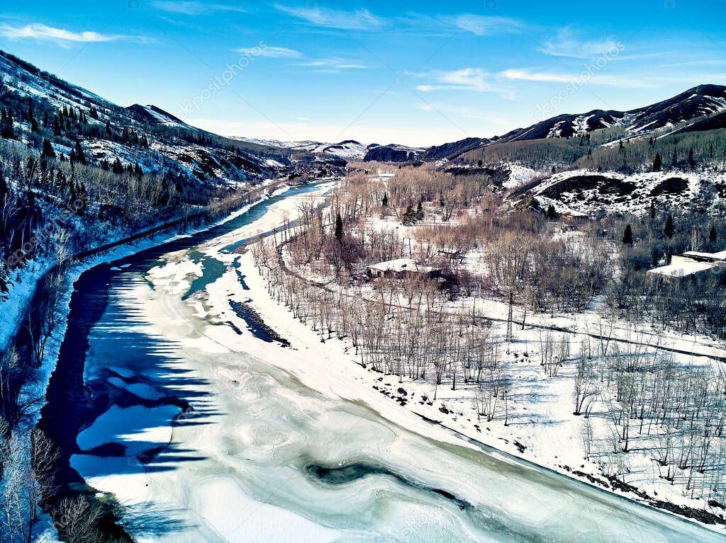 Panoramic aerial view: beautiful spring landscape: the Ulba river in Kazakhstan wakes up from winter sleep - ice drift - snow and ice are melting in the mountains, the bright sun is shining, Qazaqstan