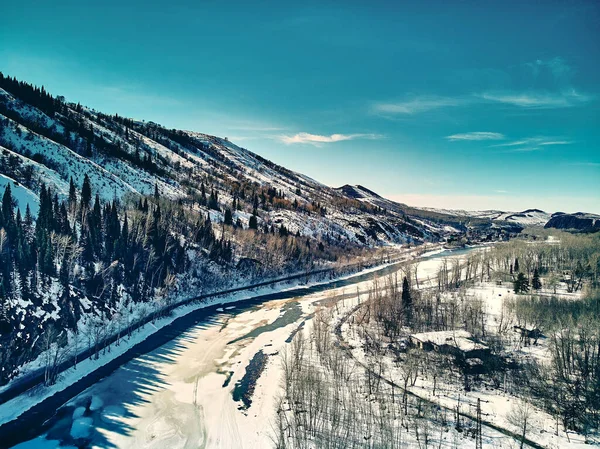 Panoramic aerial view: beautiful spring landscape: the Ulba river in Kazakhstan wakes up from winter sleep - ice drift - snow and ice are melting in the mountains, the bright sun is shining, Qazaqstan