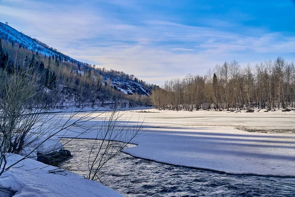 Panoramic view: beautiful spring landscape: the Ulba river in Kazakhstan wakes up from winter sleep - ice drift - snow and ice are melting in the mountains, the bright sun is shining, Qazaqstan