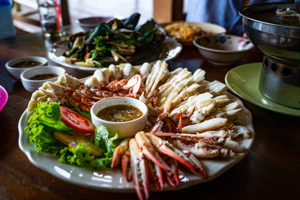Steamed meat of Blue Swimming Crab with claws, vegetables and Thai style sauce in white dish on a wooden table.
