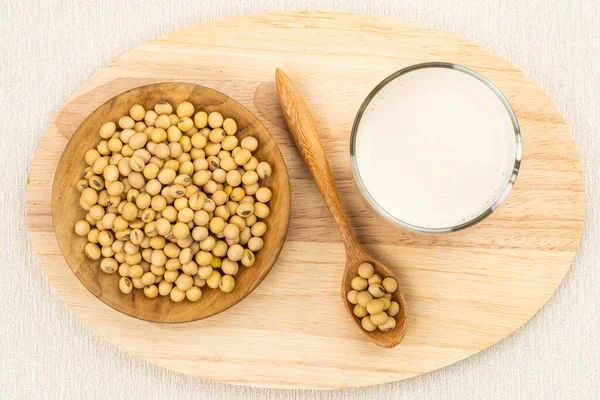 Top view of soybean milk in a glass with soy beans in wooden plate and in wooden spoon on wooden board.