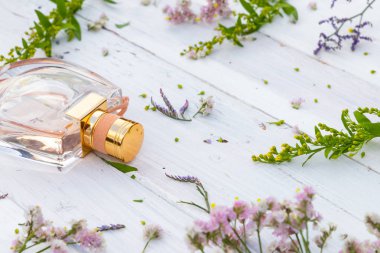 Ahşap arka planda taze çiçeklerle çevrili parfüm şişesi