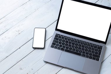 Laptop ve beyaz ahşap masadaki boş ekranlı telefon. Çalışma alanı. Boşluğu kopyala.